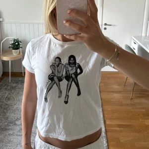 Vit t-shirt med grafiskt tryck - Vit t-shirt med ett svartvitt grafiskt tryck av två sittande personer på framsidan. Modellen är klassisk med rund hals och korta ärmar. T-shirten är i mjuk bomull och har en avslappnad passform som känns chill och enkel att styla.