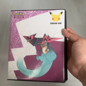 Pokémon Trading Card Game 25th Anniversary Samlarpärm - Cool samlarpärm med Pokémon-motiv och flera sidor fyllda med färgstarka och glittriga Pokémonkort! Perfekt för dig som älskar att samla, byta och spela Pokémon TCG. En grym start eller tillägg till din samling – visa upp dina favoriter och håll dem i toppskick!