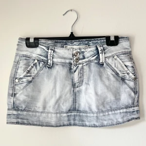 Ljus jeanskjol med slitna detaljer - Snygg ljusblå jeanskjol i kort modell med slitna tvättade detaljer. Kjolen har dubbla knappar framtill, bälteshällor och fyra fickor med nitar. Perfekt för dig som gillar en cool och avslappnad stil. 