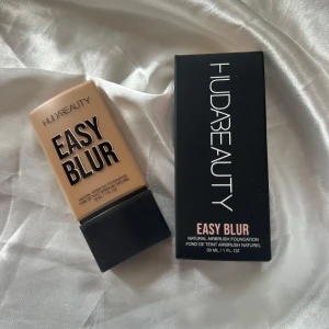 HUDA BEAUTY Easy Blur Foundation 310G - HUDA BEAUTY Easy Blur Foundation i nyansen Amaretti 310G. Kommer i en snygg beige plastflaska med svart lock, 30 ml. Ger en naturlig airbrush-effekt och innehåller 1,5% niacinamid. Perfekt för dig som vill ha en jämn och flawless bas.