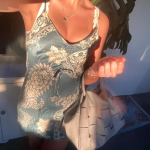 Mönstrad kortklänning från Zara - Supersöt kortklänning från Zara i turkosblått och beige med paisley- och blommönster. Klänningen har smala axelband, v-ringning och snörning framtill. Materialet är mjukt och svalt, perfekt för varma dagar.