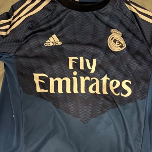 Real Madrid målvaktströja Casillas - Snygg blå Real Madrid målvaktströja från Adidas med Iker Casillas och nummer 1 på ryggen. Tröjan har lång ärm, klassiska vita Adidas-ränder på axlarna och klubbmärke samt sponsortryck framtill. Tillverkad i lätt och ventilerande material.