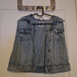 Jeansväst från Tutti Frutti Vintage - Snygg ljusblå jeansväst från Tutti Frutti Vintage med klassisk krage, knappar framtill och två bröstfickor med lock. Västen har en rak passform och coola sömdetaljer som ger en retro känsla. Perfekt att slänga över en hoodie eller t-shirt.