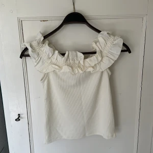 Vit söt volangtopp  - Supersöt vit topp från Cubus med bred volang runt hela axelpartiet. Toppen är i ett lite ribbat material och  är ju perfect nu till sommaren till ett par shorts eller en kjol. Toppen är oanvänd.