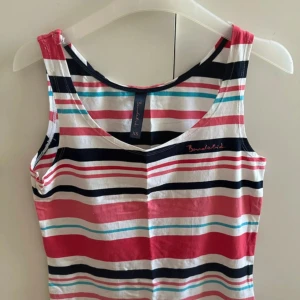 Randig linnetopp från Bondelid - Säljer en färgglad randig linnetopp från Bondelid. Toppen har breda axelband, v-ringning och är ärmlös. Mönstret består av ränder i vitt, rött, svart, rosa och turkost. Perfekt för dig som gillar en sportig och avslappnad stil