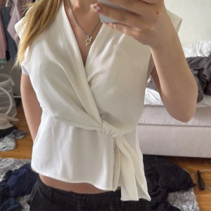 Vit omlottopp från Zara - Säljer en stilren vit omlottopp från Zara i storlek XS. Toppen har en snygg knytning i sidan, v-ringad omlottfront och är ärmlös. Perfekt för dig som gillar en clean och chic look. Materialet känns lätt och luftigt. Med knytning