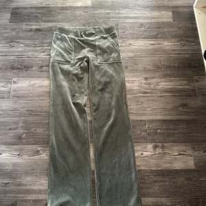 Gröna velourbyxor Juicy Couture XS - Mysiga gröna mjukisbyxor från Juicy Couture i velour med bred resår och snörning i midjan. Byxorna har raka ben, stora fickor fram och bak med knappdetaljer samt broderad JC-logga på ena fickan. Perfekta för en chill och trendig look. Aldrig använda 