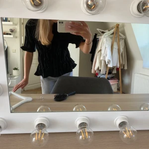 Svart blus med volang från Zara - Supersnygg svart blus från Zara med volangdetaljer och knappar framtill. Blusen har korta ärmar, v-ringning och är gjord i ett lätt, krinklat tyg som ger en cool struktur. Så söt inför sommaren!🥰