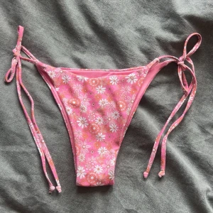 Rosa blommiga bikiniunderdel  - Supersöt bikiniunderdel i rosa med blommigt mönster och knyt i sidorna. Sitter snyggt på höften och har smala band för justerbar passform.🌸🌼