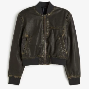 Mörkgrön skinn bomberjacka med dragkedja - Cool mörkgrön bomberjacka i skinnimitation från H&M. Jackan har ribbade muddar, dragkedja framtill och flera fickor med dragkedjedetaljer. Perfekt för dig som vill ha en edgy och stilren look. Helt ny med prislapp på!