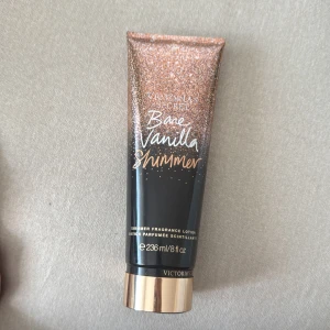 Victoria's Secret Bare Vanilla Shimmer - Glittrande shimmer lotion från Victoria's Secret i doften Bare Vanilla. Tuben är svart och guld med skimrande glitterdetaljer och rymmer 236 ml. Ger huden en snygg glow och doftar söt vanilj. Perfekt för dig som vill ha extra lyster till huden.