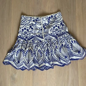 Vit och blå mönstrad kjol från Zara - Supersöt vit kjol från Zara med blått, detaljerat mönster och volangkant. Perfekt för sommaren!! Skriv vid frågor💕 Skicka prisförslag