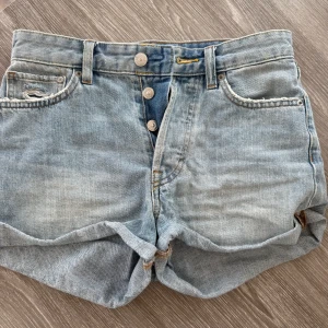 Midwest ljusblå jeansshorts &Denim - Snygga midwaist jeansshorts från &Denim i ljusblå tvätt. Klassisk femficksmodell med knappar framtill, uppvikta benslut och slitna detaljer på fickorna för en cool look. Perfekta för sommaren och lätta att matcha med allt.