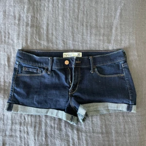 Mörkblå lågmidjade jeansshorts - Snygga mörkblå jeansshorts från Abercrombie & Fitch med låg midja. Perfekta för sommaren och sitter jätte skönt på mig som vanligtvis har storlek 38/M. De är vintage och finns inte att köpa längre och färgen passar till allt.