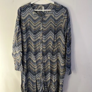 Mönstrad långärmad blus Soyaconcept - Snygg långärmad blus från Soyaconcept med vågigt mönster i blått, beige och vitt. Knappstängning framtill och rund halsringning. Tillverkad i mjuk viskos som känns skön mot huden. Perfekt för dig som gillar unika prints och bekväma plagg. Lång i modellen. Storlek M