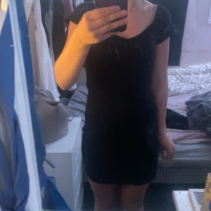 Svart ribbad kortklänning från SHEIN - Snygg svart ribbad kortklänning från SHEIN med v-ringning och korta ärmar. Klänningen är figurnära och har en offshoulder-look som ger en trendig vibe. Perfekt för dig som gillar stilrena och enkla plagg med en twist.