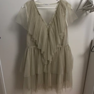 Champagnefärgad volangklänning Ida Sjöstedt - Superfin champagnefärgad kortklänning från Ida Sjöstedt, modell Aurora Dress. Klänningen har flera lager volanger i tunn mesh, v-ringning både fram och bak samt korta ärmar. Tillverkad i polyester med glansig insida. Aldrig använd ändast provad. Nypris ca 3999