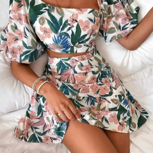 Blommig kortklänning med puffärm - Superfin kortklänning med blommigt mönster i vitt, rosa, grönt och blått. Klänningen har puffiga korta ärmar, öppen rygg och markerad midja med cut-out-detalj. Perfekt för sommarens alla tillfällen och ger en fräsch vibe.