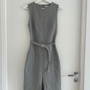 Grå klänning från Mango Suits - Snygg grå långklänning från Mango med diskret mönster, ärmlös design och tillhörande bälte i midjan. 