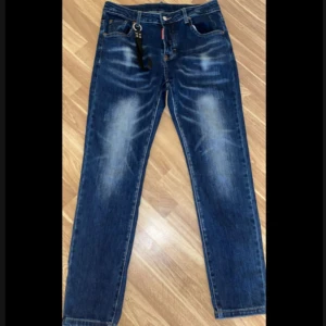 Blå Dsquared2 jeans med detaljer - Snygga blå jeans från Dsquared2 med slitningar och ljusa partier framtill och baktill. Klassisk femficksmodell med Dsquared2-logga på fickan och en cool svart nyckelring i midjan. Patch bak med 'Since 1964'. Raka ben och normal passform.