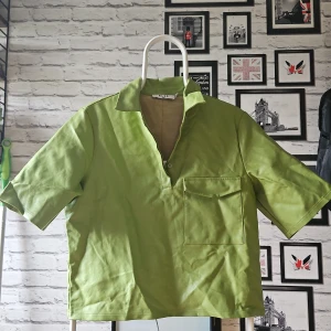 Grön kortärmad skjorta från NA-KD - Snygg ljusgrön skjorta från NA-KD med korta ärmar, klassisk krage och stor bröstficka. Skjortan har knappar längs ryggen. Perfekt för dig som vill sticka ut med en cool färg. Extra knapp medföljer 