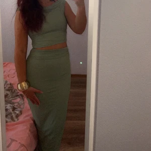 Grön långklänning med crop top - Snygg grön långklänning med matchande crop top. Klänningen har ärmlös design och tight passform som framhäver figuren. Perfekt för dig som vill sticka ut med en modern och stilren look.