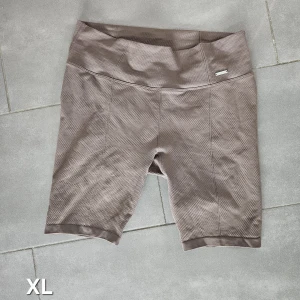 Bruna cykelshorts i XL - Snygga bruna cykelshorts i XL med hög midja och diskret struktur i materialet. Perfekta för träning eller chill dagar. Bekväm passform och stretchigt tyg som ger bra rörelsefrihet.