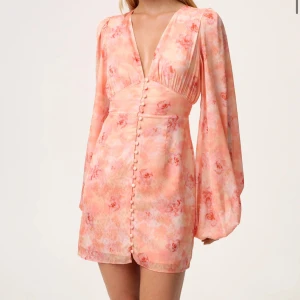 Adoore klänning - KAN POSTA IDAG!! Superfin kort klänning från Adoore i ljusa persiko- och rosa toner med blommigt mönster. Djup v-ringning, långa puffärmar och knappar framtill. Sitter snyggt i midjan och har flowy ärmar för en romantisk vibe. (ANVÄND 1 GÅNG, därav priset).💕💕Finns inte i lager hos adoore 