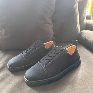 Mörkblå sneakers från Louboutin - Snygga mörkblå sneakers från Christian Louboutin i mocka med klassisk röd sula och diskret broderad logga på hälen. Skorna har svarta snören, rund tå och beige skinnfoder för extra lyxig känsla. Perfekta för dig som vill sticka ut med stil. Fler storlekar finns
