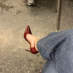 Vinröda klackskor i lack med ankelrem från Zara - Snygga vinröda klackskor i lack från Zara med spetsig tå och hög klack. Skorna har en ankelrem med resår så att den passar flera storlekar med silverfärgat spänne och stilren design! Använda en gång🤗