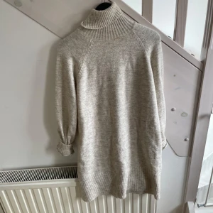 Beige polotröja i stickat material - Mysig beige polotröja i stickat material med lång ärm och bred ribbad mudd vid hals, ärmslut och nederkant. Tröjan har en loose passform och är perfekt för lager-på-lager-stil under kyliga dagar.