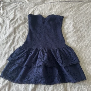 Marinblå axelbandslös klänning Gina Tricot - Säljer en utsåld söt marinblå kortklänning från Gina Tricot med smockad överdel och volangig kjol. Är i storlek L men passar mig som är en S men den sitter ändå lite löst på mig. Klänningen är axelbandslös och har broderade blommor på kjolen för en extra detalj. Perfekt för varma dagar när du vill känna dig både chill och stylish. Har bara haft på mig 1 gång.