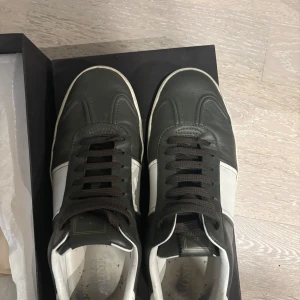 Valentino Garavani sneakers i skinn - Snygga sneakers från Valentino Garavani i mörkgrönt och vitt skinn. Skorna har svarta snören, coola nitar på hälen och en unik sula med camouflage-mönster. Valentino Flycrew läder. Skick 8,5/10, 2 nitar borta, se bild. Medföljer box och dustbag. Storlek 44 passar 45. 