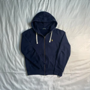 Polo RalphLauren zipper  - Polo Ralph Lauren Hoodie med Dragkedja – Mörkblå 👕 Storlek: S 🎨 Färg: Mörkblå  Snygg och tidlös hoodie från Polo Ralph Lauren i en klassisk mörkblå färg. Dragkedja framtill, två fickor och den ikoniska broderade loggan på bröstet. Skön passform i mjuk bomullsblandning – perfekt för både vardag och avslappnade outfits. Använd men i mycket fint skick, inga skador eller fläckar. Äkta vara från djur- och rökfritt hem.  ✅ 100% äkta Ralph Lauren ✅ Praktisk med dragkedja & fickor ✅ Snygg mörkblå färg