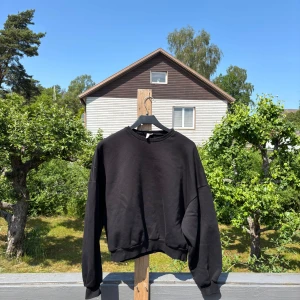 Svart sweatshirt från NELLY Trend - En svart sweatshirt från NELLY Trend i storlek S. Tröjan har en klassisk rund halsringning, ribbade muddar och är inte croppad men kortare i modellen