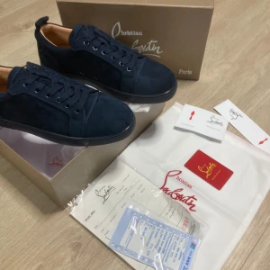 Mörkblå sneakers från Christian Louboutin - Exklusiva mörkblå sneakers i mocka från Christian Louboutin med ikonisk röd sula och rund tå. Skorna har snörning och diskreta detaljer, perfekt för dig som vill sticka ut med stil. Levereras med originalkartong, dustbag och certifikat.