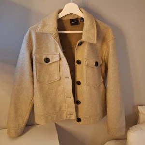Beige kappa från Vero Moda - Säljer en snygg beige kappa från Vero Moda med stora knappar och två bröstfickor. Jackan har en klassisk krage och är perfekt för höst och vår. Den är långärmad och har en stilren design som passar till många olika outfits. Passar mig som brukar ha storlek S! 💞