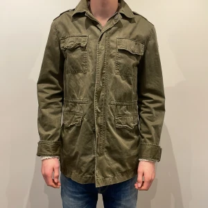 Olivgrön jacka med amerikansk flagga - Säljer en olivgrön jacka från Polo Ralph Lauren med en amerikansk flagga på ärmen. Jackan har flera fickor framtill och en klassisk krage. Perfekt för en avslappnad stil. Jackan är i storlek XL i barnstorlek men jag skulle säga att den är mellan S och M. Säljer jackan för 999 men pris kan såklart diskuteras😀