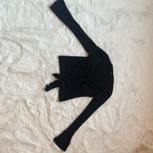 Svart långärmad topp med knyt - Snygg svart långärmad topp med knyt framtill. Perfekt för en stilren look. Passar bra till jeans eller kjol.