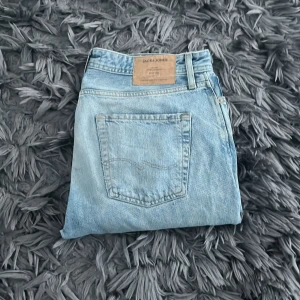 Ljusblå jeans från Jack & Jones - Säljer ett par ljusblå jeans från Jack & Jones. De har en klassisk femficksdesign och en knappgylf. Jeansen har ett litet hål på baksidan men kan enkelt sys ihop igen.