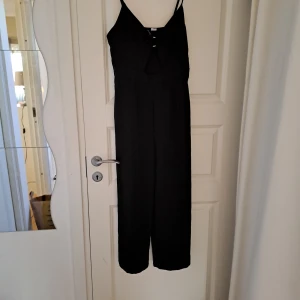 Svart axelbandslös klänning - Snygg svart axelbandslös klänning med en elegant ringdetalj framtill. Perfekt för en stilren look. Klänningen har en lång passform och är tillverkad i ett mjukt material.