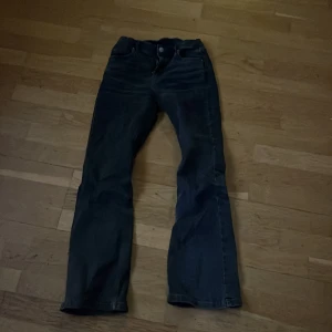 Svarta jeans från Kappahl - Snygga svarta jeans från Kappahl med hög midja och bootcut-stil. Perfekta för en trendig look. De har en klassisk femficksdesign och stängs med knapp och dragkedja framtill.