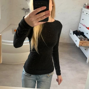 Svart glittrig intimissimi tröja - Säljer en svart långärmad tröja med en tight passform. Tröjan har ett diskret glittrigt mönster som ger en extra touch. Perfekt för att lägga till lite stil i vardagslooken. tröjan kommer ifrån intimissimi och har använt den max 2 gånger så skulle säga att den är i nyskick