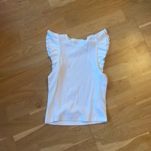 Vit ribbad topp från Kappahl - Säljer en söt vit ribbad topp från Kappahl med volangdetaljer vid ärmarna. Den är supersöt och passar till allt! 🌼kom privat vid frågor❤️