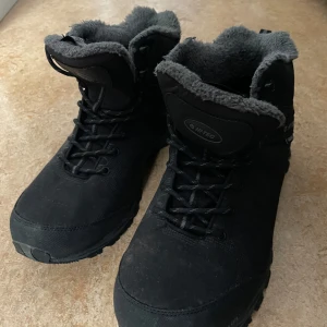 Svarta vinterkängor från Hi-Tec - Säljer ett par svarta vinterkängor från Hi-Tec med grått foder. Kängorna har snörning och är vattentäta med Thinsulate-isolering för extra värme. Perfekta för kalla och blöta dagar. 