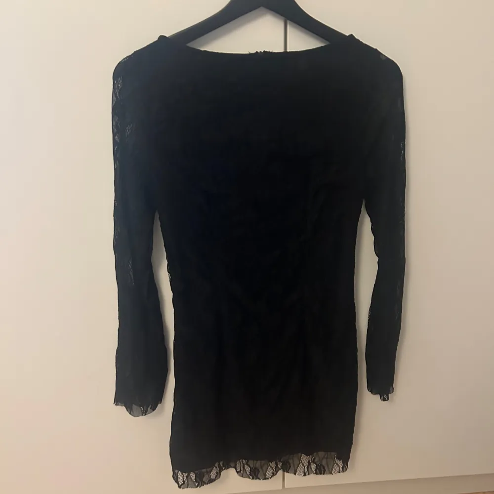 Elegant svart klänning med spetsdetaljer och långärmad design. Perfekt för en stilren look med en touch av romantik. Klänningen har en figurnära passform och är tillverkad i ett mjukt material som ger en bekväm känsla. Stolek M, men passar även S. Mekot.