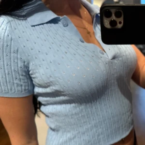 Ljusblå ribbad polotopp - Säljer en ljusblå ribbad polotopp med korta ärmar och en klassisk krage. Toppen har en v-ringad design och är perfekt för en stilren look. Passar bra till både jeans och kjol.