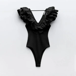 Zara body  - Snygg svart bodysuit med djup v-ringning och volangdetaljer runt halsen. Perfekt för en stilren och elegant look. Skriv om ni vill ha fler bilder💕
