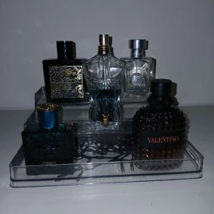 Parfymkollektion med olika märken - En samling av exklusiva parfymer från olika märken. Flaskorna har unika och eleganta designer, inklusive en med en mörk, mönstrad yta och en annan med en genomskinlig, skulptural form. Perfekt för den som vill ha en varierad doftgarderob.