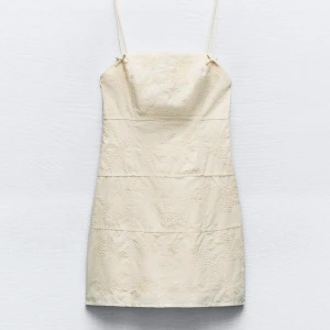 Vit broderad klänning med smala axelband - Säljer en super gullig beige/vit klänning med smala axelband och broderingar. Klänningen har små rosetter vid axelbanden och en kort längd. Aldrig använd med prislapp kvar💕🥂